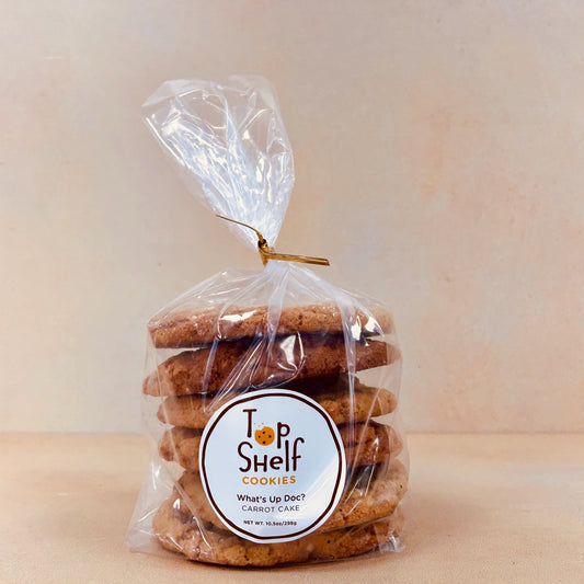 A clear plastic bag containing several cookies, sealed with a twist tie at the top. A label on the front of the bag reads 'Top Shelf Cookies, What's Up Doc?' indicating the product name and variety.