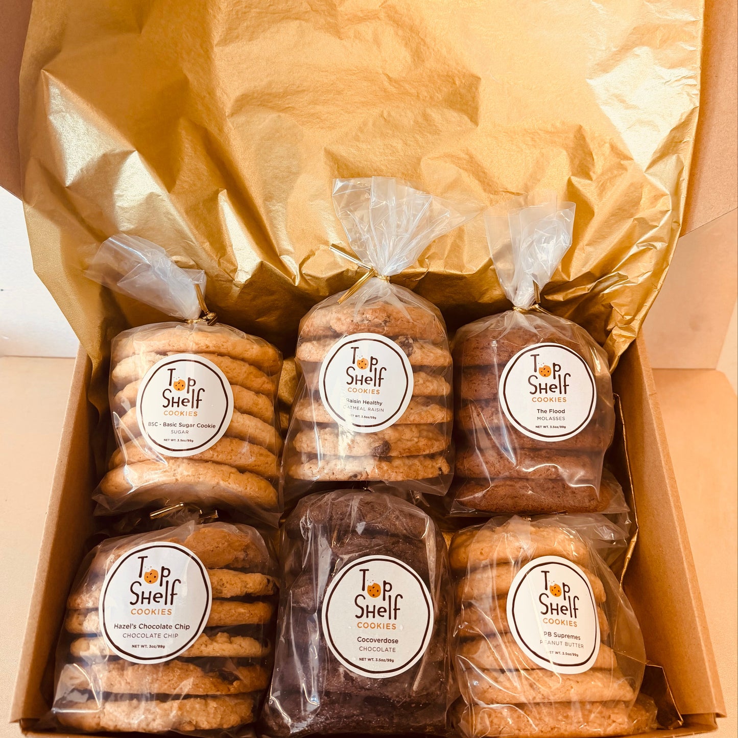 Box of bagged snacks with 'Top Shelf' labels on a neutral background