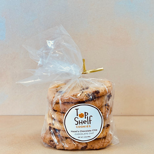 Packaged chocolate chip cookies with a label that reads 'Top Shelf Cookies - Hazel's Chocolate Chip'.